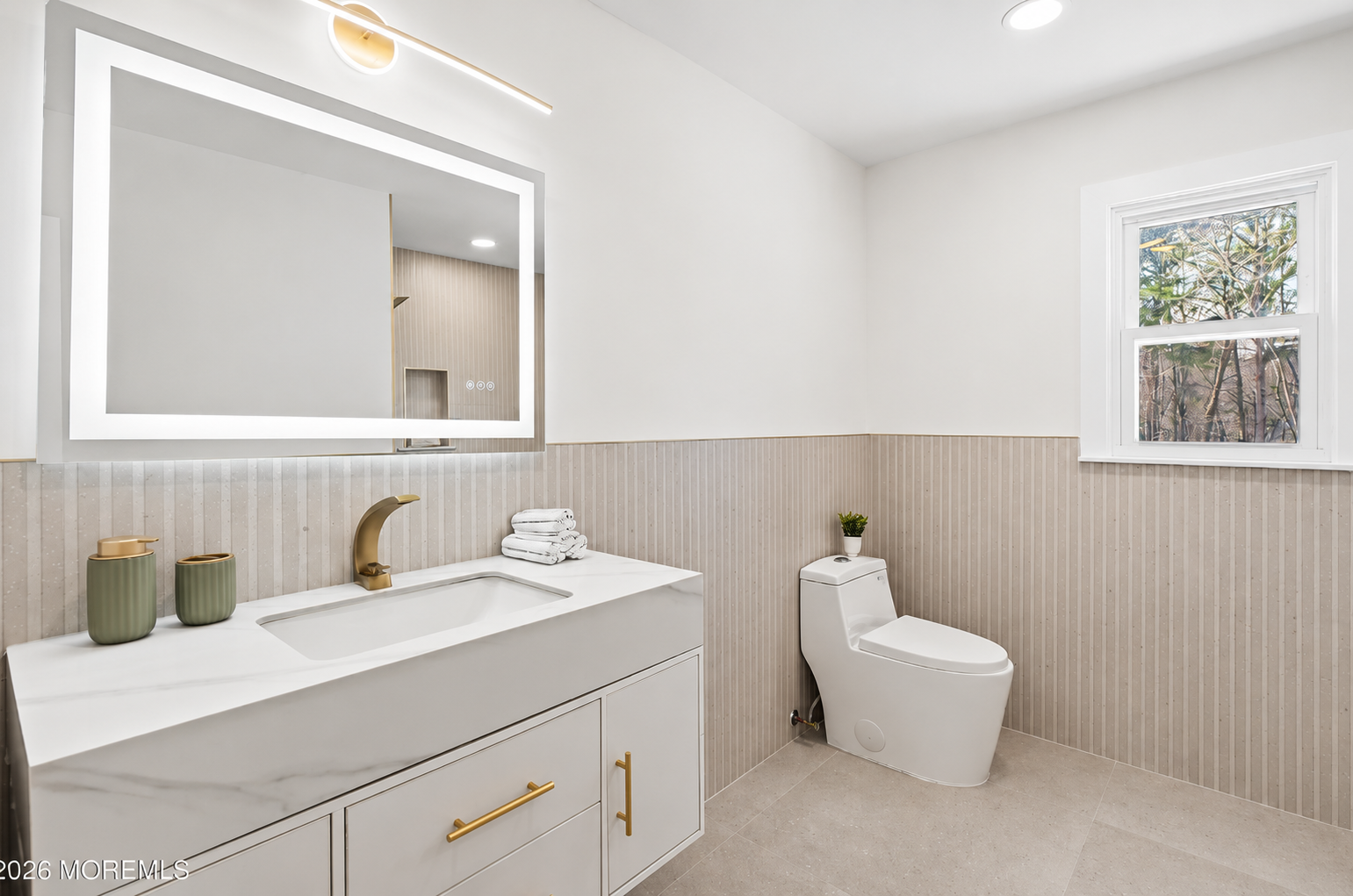 Renovated bathroom with fluted wainscot, backlit mirror, and brass fixtures